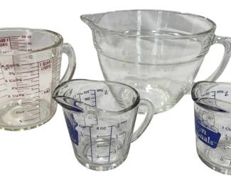 1243 - Glass Measuring Cups Collection (4) (Description): Collection of four glass measuring cups in  assorted sizes. The set includes a large  Pyrex 4-cup measuring cup with red  measurement markings, an Anchor Hocking 8-cup  batter bowl with handle and pour spout, and two smaller 1-cup measuring cups featuring  blue measurement markings and graphics. All  pieces feature easy-to-read graduated  measurements in cups, ounces, and metric  units, with sturdy handles for comfortable