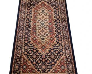 3988 - Machine Made Rug 25.5"x56" (Description): Machine made rug featuring a traditional  Persian-inspired design with a central  medallion field in cream and rust tones. The  rug displays an intricate geometric and  floral pattern with multiple decorative borders in navy blue, rust, cream, and pink  hues. Natural fringe at both ends.
