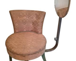 3712 - Vtg Vanity Chair w/ Attached Swivel Mirror (Description): Vintage vanity chair with attached swivel  mirror. The chair features pink damask  upholstery with a floral pattern and  button-tufted back. The asymmetrical design  includes a curved metal arm supporting an oval rotating mirror. The chair rests on  tapered fluted wooden legs with a painted  green finish. Measures 40" x 19" x 17".
