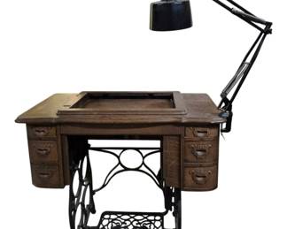 4084 - Vtg Singer Treadle Sewing Table w/ Cast Iron (Description): Vintage sewing table without machine. This  oak cabinet features a Singer treadle base  with ornate cast iron scrollwork and foot  pedal. The wooden cabinet includes six  drawers with decorative carved pulls, three on each side. The top has a recessed center  section where the sewing machine would have  been housed. A black articulating desk lamp  is attached to the right side of the table.  The piece exhibits age-appropriate wear