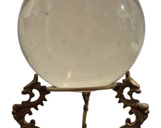 4051 - Magic Crystal Ball on Dragon Stand (Description): A magic crystal ball presented on an ornate  brass dragon stand. The clear glass sphere  rests atop a decorative tripod base featuring  three stylized dragon figures with scrolling  forms. The stand has a triangular brass base supporting the mythical creature motifs that  elegantly cradle the crystal ball.