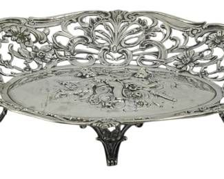 84 - German Silver Repousse Dish 3.5"x13"x8" (Description): German silver repousse dish featuring ornate  pierced decoration with scrolling floral and  foliate motifs. The oval form rests on four  decorative feet and is fitted with curved  handles at each end. The center displays repousse floral designs. Measures