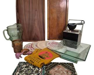 3972 - Mid Century Group Lot Decorative Items (Description): Mid Century group lot featuring an assortment  of decorative and functional items. The  collection includes a large walnut serving  tray with handles, a wooden rectangular box,  a chrome and black table lighter, a Coca-Cola embossed glass pitcher with wicker holder,  decorative crocheted doilies, green glass  square plates, decorative ceramic tiles with  floral and geometric patterns, a pink ceramic  elephant figurine, and a vintage Garfield