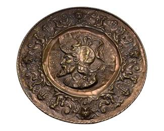 1190 - Large Copper Charger 21.5" (Description): Large copper charger featuring elaborate  repousse decoration. The center displays a  profile portrait of a classical warrior  figure wearing a plumed helmet, with the word  "MARS" visible. The wide rim is decorated with scrolling acanthus leaves, grotesque  masks, and mythological motifs. Measures 21.5  inches in diameter.