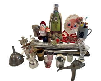 579 - Barware Collection w/ Cocktail Accessories (Description): An assorted collection of barware items and  accessories. The lot includes a metal funnel,  silver-toned egg cup, horn shot glass,  decorative shot glasses, metal jigger, glass  cocktail shaker with metal lid, Turkish kebab skewers in original packaging, bottle  jewelry accessory in packaging, various  cocktail picks and stirrers, decorative Santa  ornaments, a blue stoneware mug with various  swizzle sticks, metal bird-shaped bottle