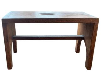 1411 - Wooden Stool 10"x15.5"x7.5" (Description): Wooden stool featuring a simple design with a  handle cutout on the top surface and a  stretcher bar between the legs.
