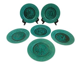 373 - 6 French Majolica Dessert Plates 8" (Description): A set of six glazed plates, each measuring 8  inches in diameter. The plates feature a teal  green glaze with a decorative basketweave  pattern on the rims and various fruit and  floral motifs in the centers.