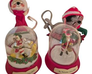 4060 - 2 Enesco Snow Globes & 2 Annalee Dolls (Description): A charming collection featuring two Enesco  St. Nicholas snow globes with Annalee mouse  dolls perched atop. The snow globes are  labeled "St. Nicholas circa 1905" and "St.  Nicholas circa 1910" on their red bases, each containing a miniature Santa Claus scene  under a clear dome. The accompanying Annalee  dolls include a figure with a red scarf and a  mouse character wearing a red and white  striped knit cap and green outfit on a