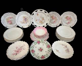 467 - Group Lot of Porcelain Plates (Description): A group lot of porcelain plates featuring  various decorative styles. The collection  includes plates with floral motifs, pierced  borders, gold trim accents, and assorted  sizes. Some plates feature delicate hand-painted rose designs while others  display embossed patterns.