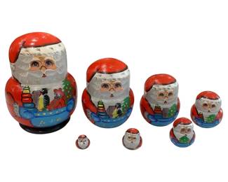 642 - Russian Santa Claus 7pc Nesting Doll Set 7" (Description): The set depicts Santa with a traditional red  suit and cap, white beard, and a festive  scene on the front showing toys, a teddy  bear, a penguin, and a Christmas tree.  Measures 7 inches tall.