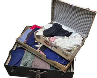 4115 - Two Vintage Trunks Filled w/ Fabric & More (Description): Two vintage trunks filled with fabric and  assorted sewing materials. The collection  includes a variety of fabric pieces in  multiple colors and patterns including blue,  red, pink, green, and floral prints. Also contains linens, lace, and other textile  items. The larger black trunk features metal  hardware and latches, while the smaller trunk  has a gingham-lined interior.