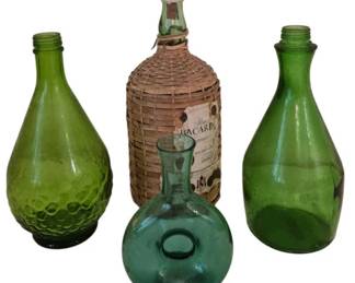 3960 - Four Green Glass Bottles Incl Wicker Wrapped (Description): Collection of four green glass bottles in  varying shades and styles. The grouping  includes a wicker-wrapped Bacardi rum bottle  with original label, a dimpled  teardrop-shaped bottle, a spherical flask-style bottle with pontil mark, and a  tall tapered bottle. Each displays  characteristic green coloring typical of  decorative glass bottles.