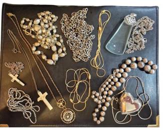 1981 - Collection of 11 Assorted Costume Necklaces (Description): A collection of eleven assorted costume  necklaces featuring a variety of styles. The  grouping includes several cross and crucifix  pendants in rhinestone and carved bone,  silver-toned bead necklaces with textured oval beads, delicate gold-toned chains, a  silver-toned link chain, a heart-shaped  pendant, and a large polished stone pendant.  The collection offers a diverse mix of  religious motifs and decorative designs