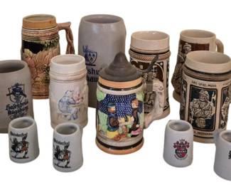 3963 - Collection of 17 German Beer Steins (Description): A collection of 17 beer steins in assorted  styles and materials. The group includes  glass steins with pewter lids, traditional  stoneware steins with relief decoration,  ceramic miniature steins, and hand-painted examples featuring German scenes and coats of  arms. Various sizes represented from  miniature shot-sized to full-sized drinking  steins.