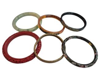 1997 - 6 Asian Bangles Incl Jade Cloisonne Cinnabar (Description): Collection of six Asian bangles featuring a  variety of materials and decorative  techniques. The assortment includes a pale  green jade bangle, a carved red cinnabar  bangle with floral motifs, a black cloisonne bangle with floral design, a  tortoiseshell-style bangle, a brass bangle  with engraved decoration, and a black enamel  bangle with gold characters.