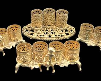 2716 - 4 Vtg Filigree Lipstick Holders Gold Tone (Description): Two vintage filigree lipstick holders in gold  tone metal. One holder features four  cylindrical compartments on a footed base  with ornate pierced detailing. Another holder  has three cylindrical compartments on an oval base with elaborate openwork floral  design. They display intricate pierced  metalwork throughout with a warm brass or  gilt finish showing attractive patina  consistent with age.