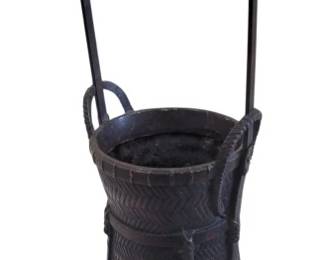 441 - Toyo Woven Iron Basket w/ Tall Handle 10" (Description): Iron basket featuring intricate woven  herringbone pattern construction with a tall  arched carrying handle. The basket has a  cylindrical upper section that tapers to a  squared base supported by four small feet. Additional small loop handles are attached at  the rim. The piece displays a dark aged  patina throughout. Measures 10 inches.