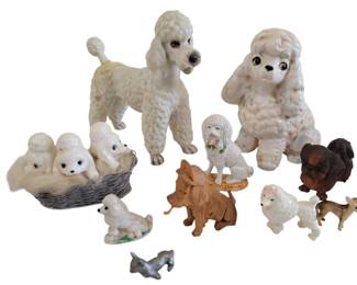 447 - Lot of Assorted Dog Statues 6.5 - 13" (Description): Lot of assorted dog statues in various sizes  and materials. The collection features  predominantly poodle figurines in white  ceramic, including two large standing and  sitting poodles, puppies in a basket, and smaller accent pieces. Also included are  carved wooden dogs, a brown ceramic  Pekingese-style figure, miniature bone china  dogs, and a small metal terrier. Sizes range  from 6.5 to 13 inches.