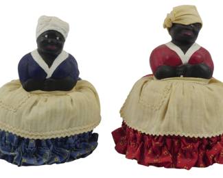 1703 - 2 Vintage Black Americana Pin Cushions 6" (Description): Two vintage Black Americana pin cushions.  Each figure features a painted composition  upper body wearing a headwrap and dress,  seated atop a fabric-covered pin cushion base  with decorative ruffled trim. Measuring 6 inches.