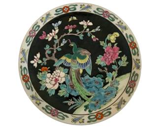 285 - Nippon Decorative Plate Round 9.75" (Description): Nippon decorative round plate featuring a  striking famille noire style design with a  central peacock perched on rockwork amid  blooming peonies and magnolia branches  against a black ground. The wide rim displays a repeating pattern of stylized ribbons,  coins, and geometric motifs on a white  background. Measures 9.75" in diameter.
