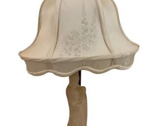 284 - Carved Asian Figural Table Lamp w/ Shade (Description): A carved Asian figural table lamp featuring a  robed figure standing on a wooden base with  decorative brass foot. The lamp includes a  bell-shaped fabric shade with floral damask  pattern and a carved finial. Measures 21.5" x 36".