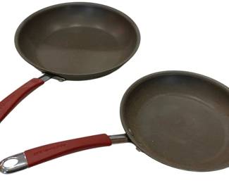 924 - Pair of Rachael Ray Skillets w/ Red Handles (Description): Two Rachael Ray skillets featuring a  bronze-colored nonstick interior and  distinctive red silicone-wrapped handles with  stainless steel accents. The pans appear to  be different sizes, suitable for various cooking tasks.