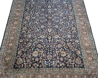 2043 - Hand-Knotted Persian Rug 107"x65" (Description): Hand-knotted Persian style area rug featuring  an intricate allover floral design on a deep  navy blue field. The central field displays  elaborate palmettes, lotus blossoms, and  scrolling vines in shades of coral, cream, blue, and green. Multiple decorative borders  frame the piece, including a wide  salmon-toned floral border and narrow guard  stripes. The rug features traditional fringed  ends & leather bound sides.