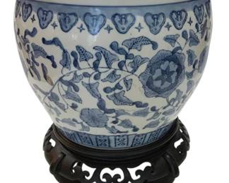 955 - Blue & White Chinese Planter on Stand (Description): Chinese blue and white porcelain flower pot  or planter with traditional floral and  foliate decoration. The vessel features  botanical motifs including flowers, leaves,  and scrolling vines, with a decorative heart-shaped border pattern around the rim.  Comes with a carved wooden display stand with  scrollwork design. Measures 13" x 10".