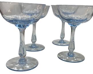 959 - 4 Light Blue Glass Stemmed Champagnes (Description): These elegant glasses feature a delicate blue  tint throughout, with graceful stems and  circular bases. The shallow, wide bowls are  characteristic of classic champagne coupes or  cocktail glasses.
