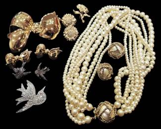 2810 - Costume Jewelry Lot Brooches Pearls Earrings (Description): A collection of costume jewelry featuring  various brooches, faux pearl necklaces, and  earrings. The lot includes a large gold-tone  bow brooch with matching bow earrings, a  rhinestone-encrusted swallow bird brooch with matching smaller bird earrings, gold-tone  sunflower cluster earrings, a poodle brooch,  and multiple strands of faux pearl necklaces  with decorative gold-tone pearl-centered  clasps. An assorted grouping suitable for