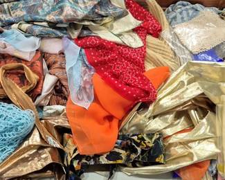 2844 - Lot of Assorted Scarves & Fabrics (Description): A varied collection of assorted scarves and  fabric pieces. The lot includes a diverse  array of colors and textures, featuring gold  lame, turquoise crocheted or netted fabric,  floral prints, solid colors in orange, red, and blue, as well as metallic and silk-like  materials. The assortment offers a range of  patterns from polka dots to paisleys and  brocade designs, suitable for crafting,  fashion accessories, or textile collecting.