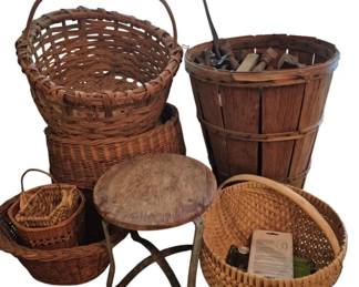 3902 - Group Lot of Woven Baskets & Wooden Stool (Description): A group lot of assorted baskets and  accessories. The collection includes several  woven baskets in various sizes and styles,  including a large handled basket, a tall  bushel-style basket, and smaller gathering baskets. Also included is a rustic wooden  stool with a round top and curved legs. The  baskets display traditional woven  construction in natural tones.