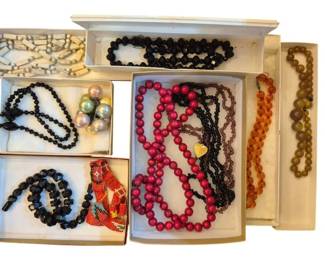 1472 - Group Vintage Beaded Necklaces (Description): A collection of vintage beaded necklaces  featuring a variety of styles and materials.  The group includes black faceted glass bead  necklaces, red wooden bead strands,  amber-colored graduated bead necklaces, a bone or ivory-toned tubular bead necklace,  and additional strands in various colors  including purple and olive tones. Also  included is a beaded accessory with Native  American-inspired red geometric pattern and