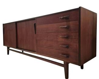 4023 - Mid Century Credenza 31"x85"x18" (Description): Mid Century credenza featuring a sleek,  low-profile design with two sliding cabinet  doors and four drawers on the right side. The  piece is crafted in a rich dark wood finish  and rests on tapered legs connected by a stretcher base. Measures 31 inches high by 85  inches wide by 18 inches deep.