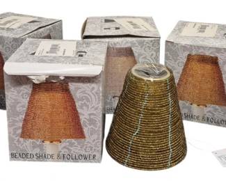 4031 - 8 Beaded Candle Shades w/ Followers in Boxes (Description): A collection of eight beaded candle shades  with followers. The shades feature a warm  amber-gold beaded construction in a classic  tapered lampshade form. Seven remain in their  original decorative gray damask-patterned boxes labeled "Beaded Shade & Follower,"  while one shade is displayed outside its  packaging showing the detailed beadwork  design.