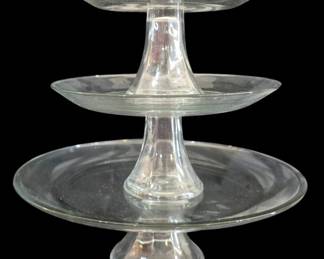 526 - Three Tiered Clear Glass Cake Stands (Description): A set of three clear glass pedestal cake  stands in graduated sizes, designed to nest  together creating a tiered display. Each  stand features a classic silhouette with a  round plate top supported by an elegant trumpet-shaped pedestal base. The  crystal-clear glass construction allows for  versatile display options. Perfect for  entertaining, dessert presentations, or  decorative purposes.