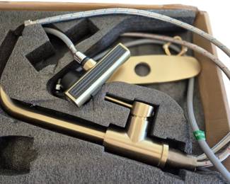 2824 - Modern Kitchen Faucet (Description): Modern single-handle kitchen faucet brushed  brass finish. The faucet features a high-arc  gooseneck spout design. Includes mounting  deck plate with soap dispenser hole and  braided stainless steel supply lines. Presented in original foam-fitted box  packaging, appearing unused or in like-new  condition. Used as is electric/electronic/mechanical  item. No guarantee all components, untested.