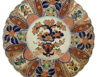 296 - Japanese Imari Porcelain Platter 12x12 (Description): Oriental plate in the traditional Japanese  Imari style, featuring a scalloped edge and  elaborate hand-painted decoration. The  central medallion displays a floral  arrangement with chrysanthemums and foliage in characteristic Imari colors of cobalt  blue, iron red, and gold. The border is  divided into alternating panels with stylized  lotus motifs, geometric patterns, and  mythical creatures. Measures 12 inches by 12