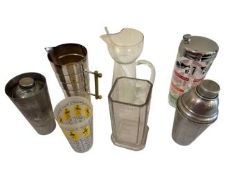 575 - Vintage Cocktail Mixers & Barware Collection (Description): A collection of vintage cocktail mixers and  barware featuring a variety of styles and  materials. The assortment includes chrome and  stainless steel cocktail shakers, a glass  pitcher with stirring rod, a clear glass measuring pitcher marked with quart  measurements, a frosted glass shaker with  yellow cocktail recipe graphics, and a  decorated glass shaker with colorful drink  recipe illustrations and chrome lid. The