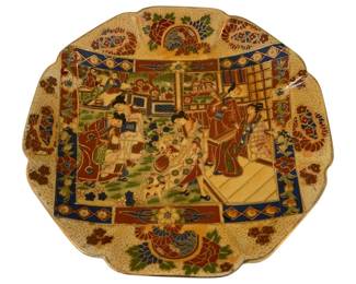 323 - Handpainted Royal Satsuma Figural Scene Plate (Description): Handpainted Satsuma plate featuring an  elaborate figural scene depicting multiple  figures in traditional Japanese dress engaged  in various activities within a garden  setting. The central scene is framed by a cobalt blue geometric border with floral  corner medallions. The scalloped rim is  decorated with peony and chrysanthemum motifs  on a cream ground with gilt accents  throughout. Measures 1.5" x 10".