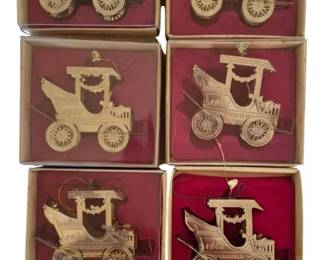 4068 - 7 Brass Vintage Car Christmas Ornaments (Description): Collection of seven brass ornaments featuring  vintage automobile designs. Each ornament  depicts an antique car with detailed spoked  wheels, canopy tops, and decorative garland  details with 'Noel' lettering. Six ornaments are presented in their original display boxes  with burgundy velvet backgrounds, while one  remains unboxed.