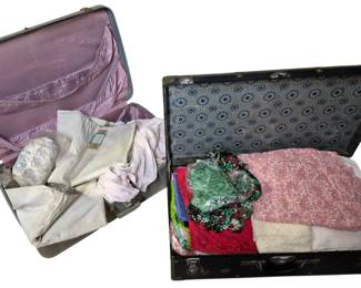 4102 - Vintage Trunk & Suitcase Filled w/ Fabrics (Description): A vintage trunk filled with an assortment of  fabrics and textiles. The trunk features a  dark exterior with metal corner hardware and  latches, and a patterned interior lining.  Contents include various fabrics in multiple colors including pink, red, green, and floral  prints, some wrapped in plastic. Ideal for  crafting, quilting, or vintage textile  collecting.