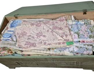4128 - Trunk of Vintage Fabric (Description): A painted wooden trunk filled with assorted  vintage fabric samples and remnants. The  collection includes various floral prints in  soft pastels and botanical patterns. The  trunk features a sage green painted exterior with visible wear consistent withage. Note:  back leg needs repair.