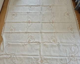 1313 - Embroidered Linen Tablecloth (Description): Features delicate needlepoint embroidery in a  scrolling floral design with cream-colored  lace edging. The ivory linen displays elegant  handwork throughout with decorative corner  motifs. Tablecloth measures approximately 87" x 69".