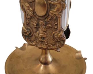 431 - Brass w/Copper Overlay Ashtray & Match Holder (Description): Ornate brass ashtray with copper overlay  featuring decorative cherub and scrollwork  motifs in relief. The piece includes a  central pedestal supporting an ornamental  holder with an oval medallion flanked by putti figures. The round base features  scalloped edges with cigar rests. Measures  4.5" x 4.5".