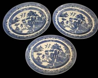 504 - 3 Johnson Bros Blue Willow Oval Platters (Description): Set of three blue and white oval platters in  the classic Blue Willow pattern. Each platter  features the traditional transferware design  depicting a Chinese landscape with pagodas,  willow trees, birds, and a bridge, surrounded by an ornate geometric and floral border.  The platters measure 14 inches by 11 inches  and display the characteristic Chinoiserie  aesthetic popular in English transferware  from the 19th century onward.