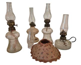 3991 - Collection of Miniature Oil Lamps (Description): A collection of miniature oil lamps featuring  various pressed glass bases with clear glass  chimneys. The assortment includes lamps with  swirled and ribbed glass patterns,  brass-toned burner fittings, and one lamp with a finger loop handle. Also included is a  small fabric lamp shade with floral print  and crocheted trim.