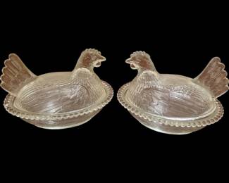 4036 - Pr Hen on Nest Covered Dishes 5"x7.5" (Description): Pair of crystal hen on nest covered dishes  featuring detailed feather patterns on the  lids and beaded edge bases. Each piece  consists of a nest-shaped base with a  removable hen-shaped lid, crafted in clear pressed glass. The hens feature upright  tails, textured plumage, and painted red comb  details.