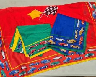 2861 - 3 Assorted Vtg Racecar Scarves (Description): Three assorted vintage racecar scarves  featuring colorful printed designs of classic  racing automobiles. The collection includes  a large red scarf with yellow border and  checkered racing flag motif, a green scarf with yellow border, and a blue scarf with  green border. Each scarf displays various  vintage race cars in multiple colors around  the borders and center fields.