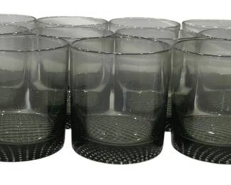 1225 - Smokey Gray Glass 3.5" Tumblers Set of 15 (Description): Set of fifteen smoky gray glass tumblers  featuring a modern minimalist design. Each  cup has a tapered cylindrical shape with a  subtle ombre effect graduating from darker  gray at the base to lighter at the rim. The bases feature a textured circular pattern  that adds visual interest and stability.